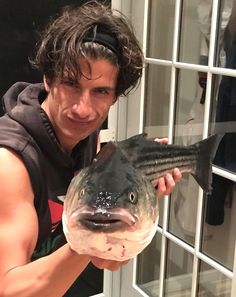 a man holding up a fish in front of a glass window with white shutters