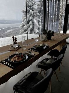 a long table with plates of food on it in front of a window overlooking the snow covered mountains