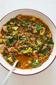 a white bowl filled with lentula and vegetables on top of a table next to a spoon