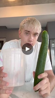 a man holding a cucumber in front of a blender