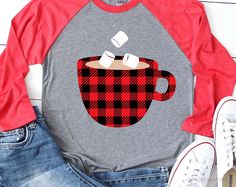 a red and black plaid coffee cup with marshmallows on it is next to some jeans