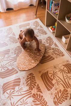 a baby is standing on a surfboard in the middle of a room with bookshelves