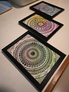 three framed art pieces sitting on top of a table