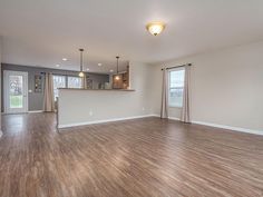 an empty living room with hard wood flooring and white walls in the kitchen area