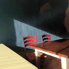 two red chairs sitting on top of a wooden table next to a blue wall and floor