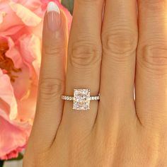 a close up of a person's hand with a ring on it and flowers in the background