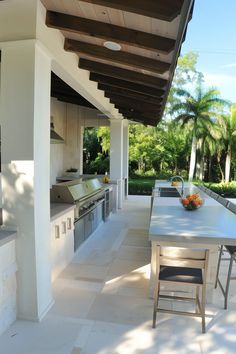 an outdoor kitchen and dining area with table, chairs and grill on the side wall