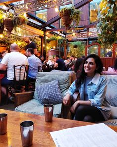 a woman sitting at a table in a restaurant with lots of people eating and drinking