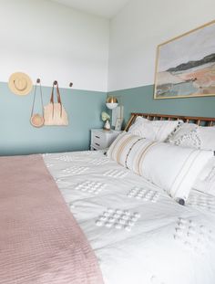 a bed with white and pink comforter in a blue room next to a painting on the wall