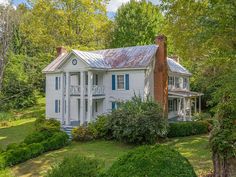 an old white house surrounded by trees and bushes