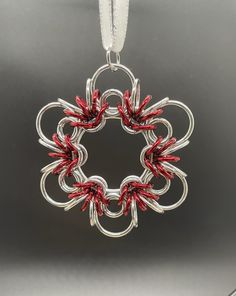 a silver and red pendant with an intricate design on it's end, hanging from a white cord