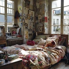 an unmade bed sitting in a bedroom next to two windows with lots of pictures on the wall