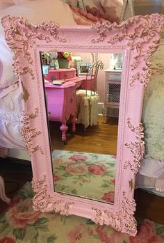 a pink mirror sitting on top of a wooden floor next to a white dresser and bed