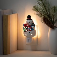 a snowman night light sitting on top of a shelf next to a pine cone