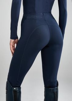 the back view of a woman in black wetsuit and riding boots, with her hands on her hips