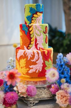 a multi - colored cake decorated with flowers on a silver platter and surrounded by other decorations