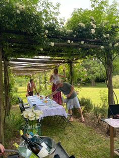 a group of people standing around a table under a pergolated area with flowers on it