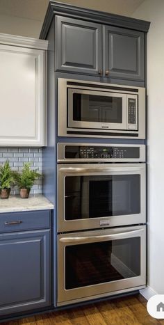 a kitchen with gray cabinets and stainless steel ovens in the wall, along with white counter tops