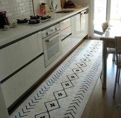 a kitchen with white cabinets and an area rug on the floor in front of the stove