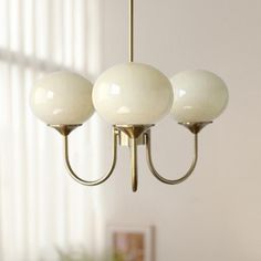 three white balls hanging from a brass chandelier in a living room with windows