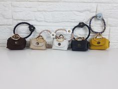 five small purses lined up against a white brick wall, all in different colors