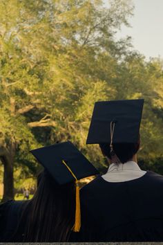 two people in graduation caps and gowns looking at the tree line with trees behind them