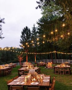 an outdoor dining area with wooden tables and lights strung from the trees, surrounded by greenery