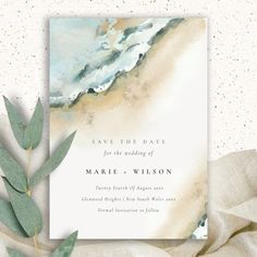 an elegant save the date card with watercolor waves and greenery on it, next to a leafy branch