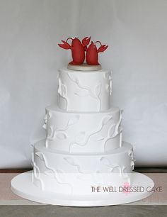 a three tiered white wedding cake with red lobsters on top and the words, the well dressed cake