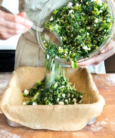 a person in an apron is sprinkling greens into a bowl