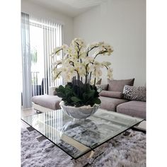 a glass table with flowers on it in front of a couch