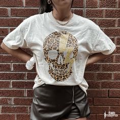 a woman standing in front of a brick wall wearing a t - shirt with a leopard print skull on it