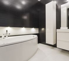 a large white bath tub sitting next to a sink in a bathroom under black and white walls