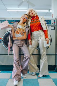 two women standing next to each other in front of a washing machine