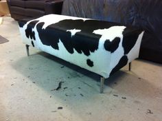 a black and white cow print bench sitting on the floor in front of a couch