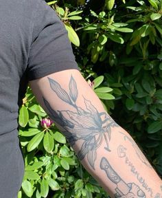 a man with a tattoo on his arm holding a cell phone in front of some bushes