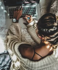 a woman sitting in front of a laptop computer on top of a white blanket covered floor