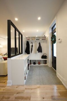 a hallway with white walls and wooden flooring next to a coat rack filled with coats