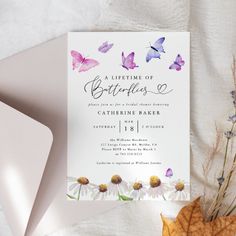 a white card with purple butterflies on it next to an envelope and some dried leaves