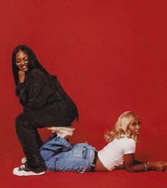 two women sitting on the ground in front of a red wall