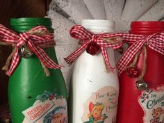 three christmas themed glass bottles with red and white bows on the top one is green