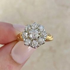 a woman's hand holding an antique diamond cluster ring in yellow and white gold