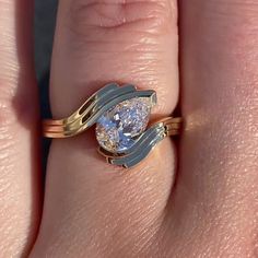 a woman's hand holding a gold and white ring with a pear shaped diamond