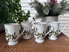 three coffee mugs with holly designs on them sitting next to a potted plant