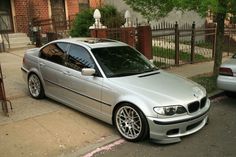 a silver car parked on the side of a street next to a sidewalk and fence