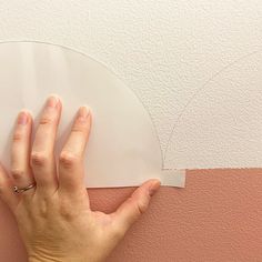 a person's hand on top of a piece of paper next to a wall