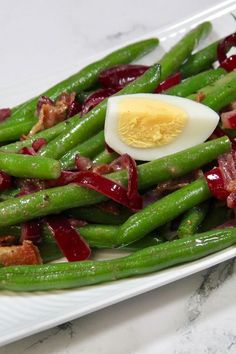 green beans with bacon and hard boiled egg on a white plate sitting on a marble countertop