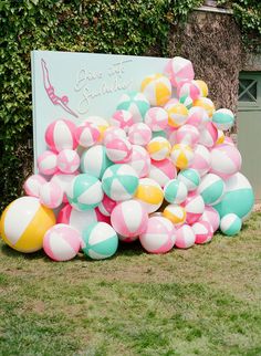 a bunch of balloons that are on the ground in front of a sign and some bushes