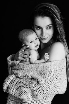 a woman is holding a baby wrapped in a blanket and posing for a black and white photo