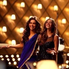 two beautiful women standing next to each other in front of a wall with lit candles